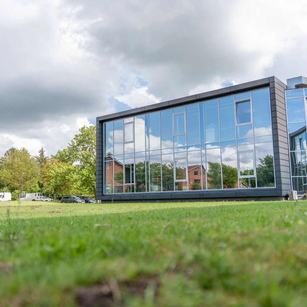 Die verspiegelte Glasfront eines modernen Bürogebäudes an einem sonnigen Tag mit Rasenfläche davor.
