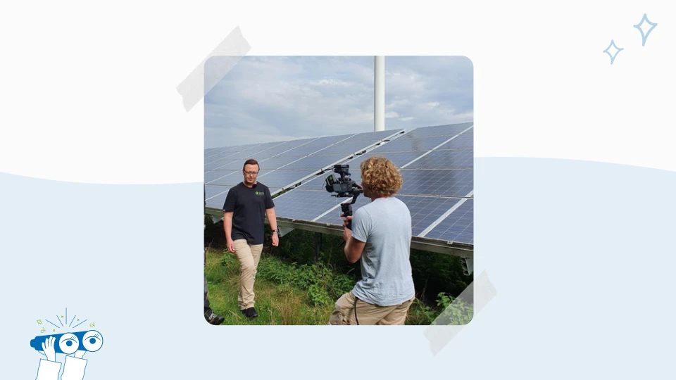 Ein Kameramann filmt einen Mann vor einer Solaranlage im Freien.