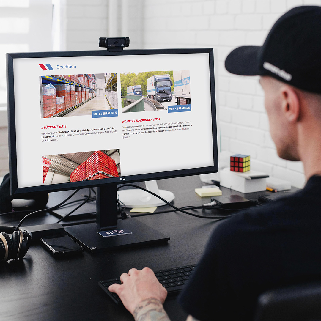 Die neue Website von Spedition Wohlert auf einem Desktop-PC. Davor sitzt ein tätowierter Mann mit Kappe am Schreibtisch. 